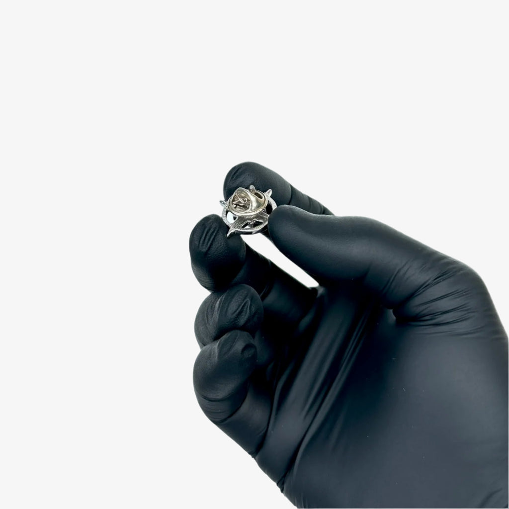 Black-gloved hand holding a diamond ring against a gray background