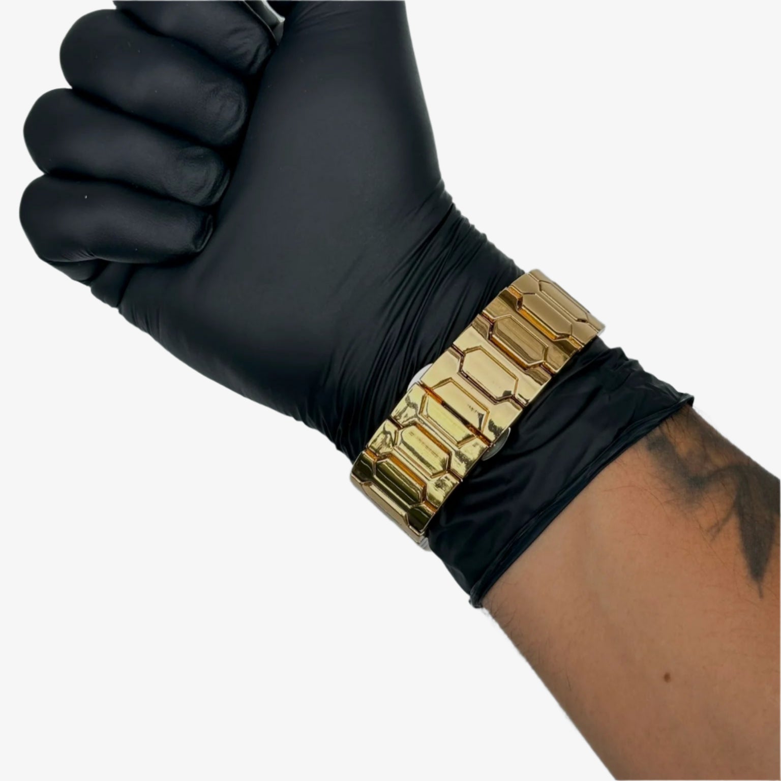 Black glove on a wrist with a gold bracelet against a gray background