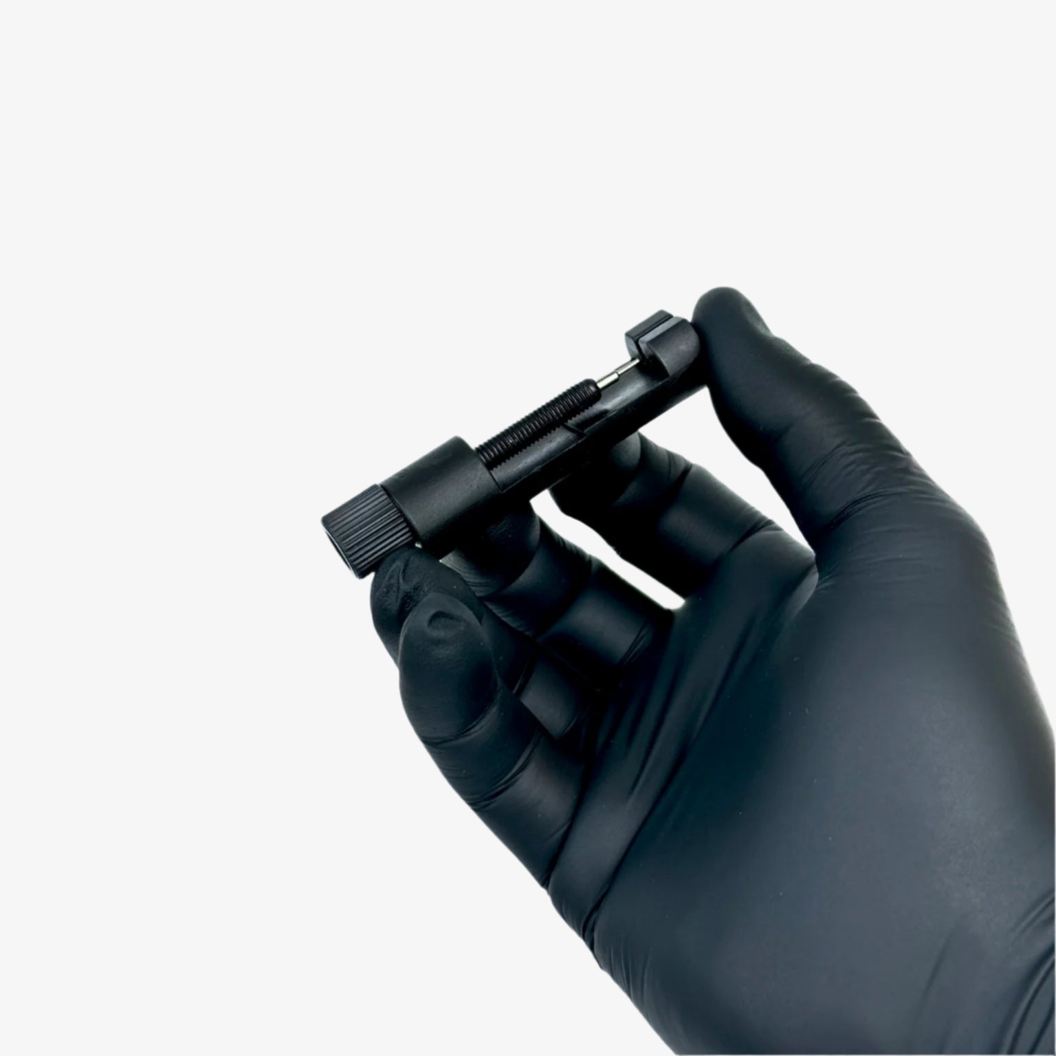 Black gloved hand holding a small black device against a light gray background