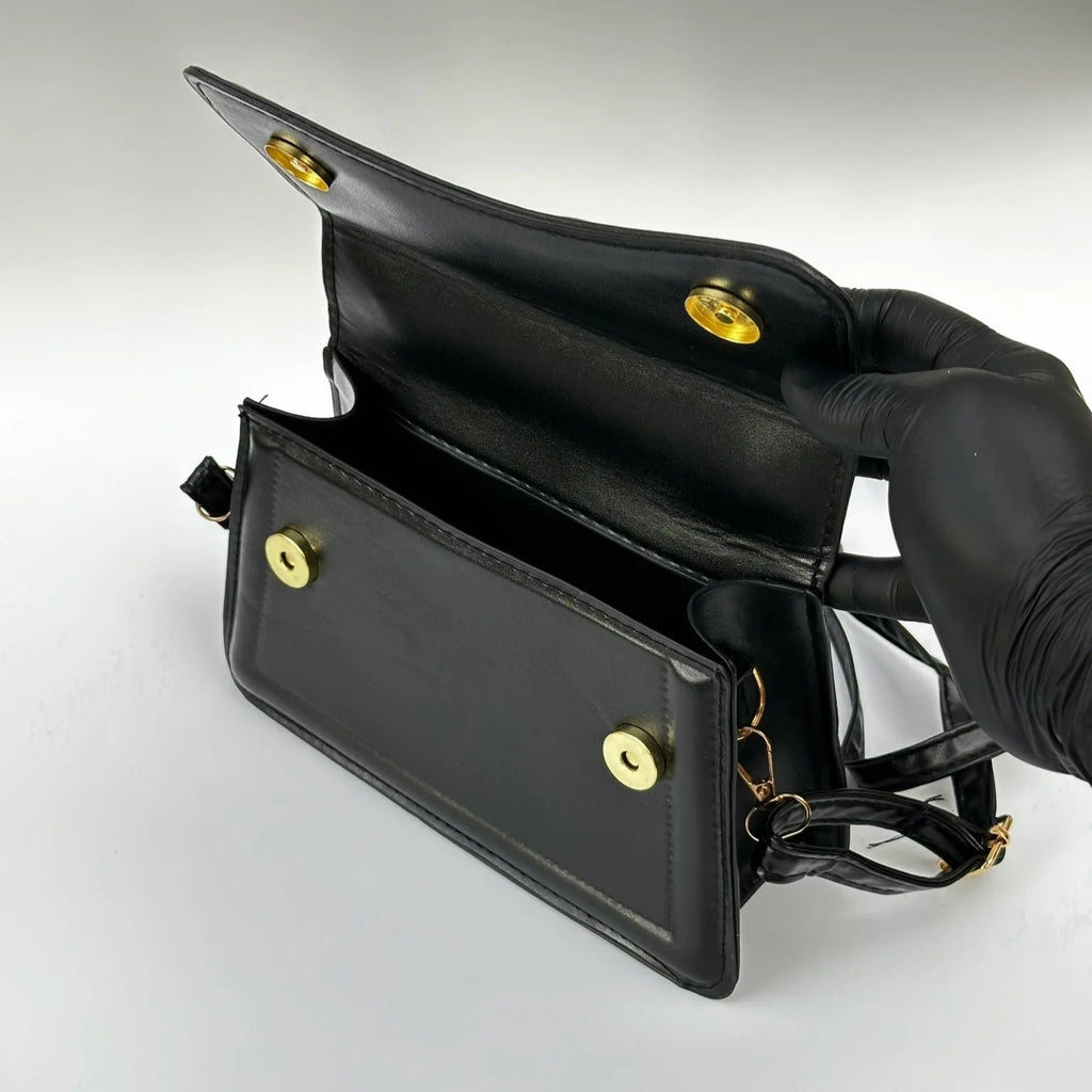 Black handbag with gold hardware held by a gloved hand on a light gray background