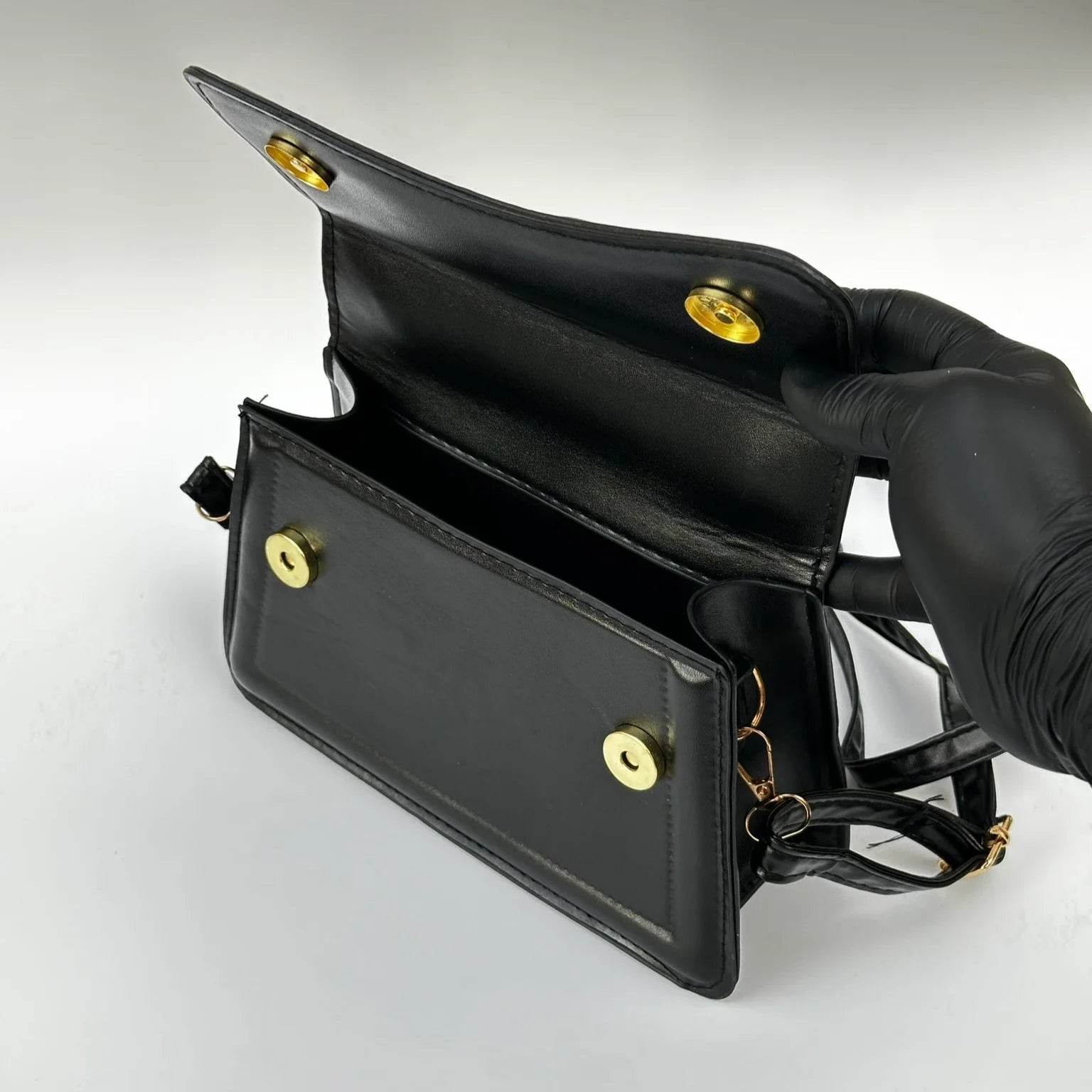 Black handbag with gold hardware held by a gloved hand on a light gray background