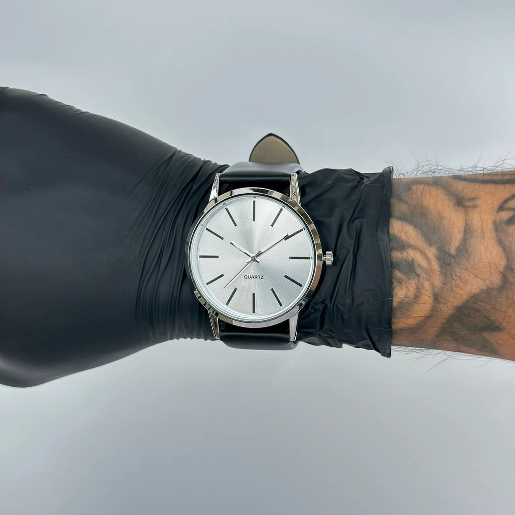 Black wristwatch on a wrist with a tattoo, against a light gray background