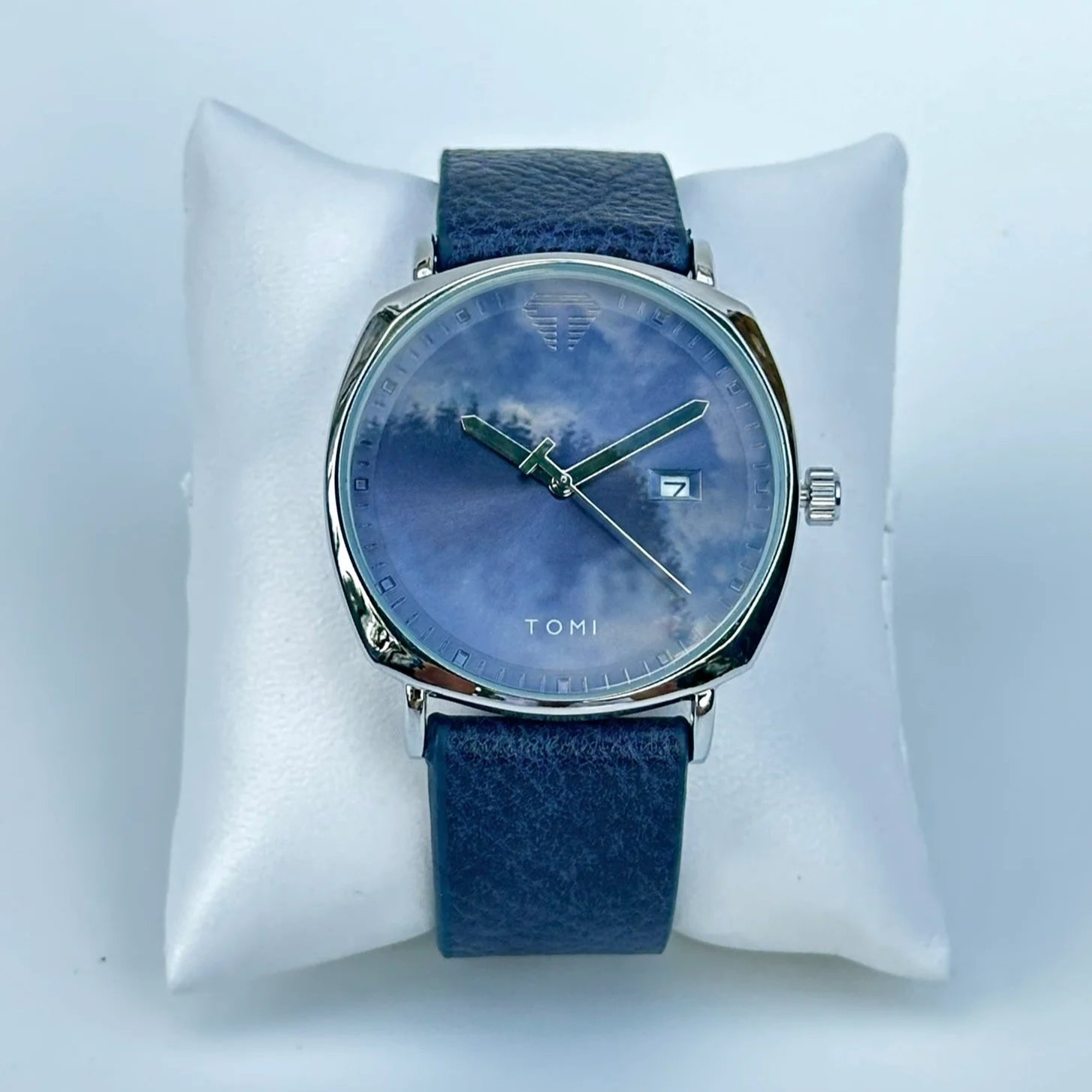 Blue watch with a blue strap on a white cushion against a light gray background