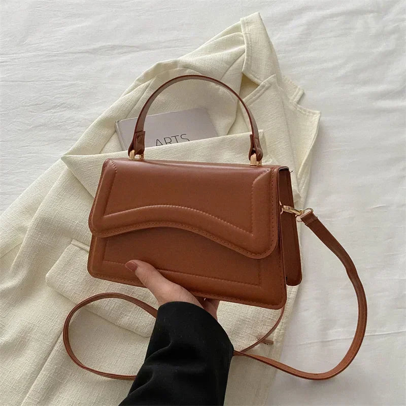 Brown handbag held by a hand on a light fabric background
