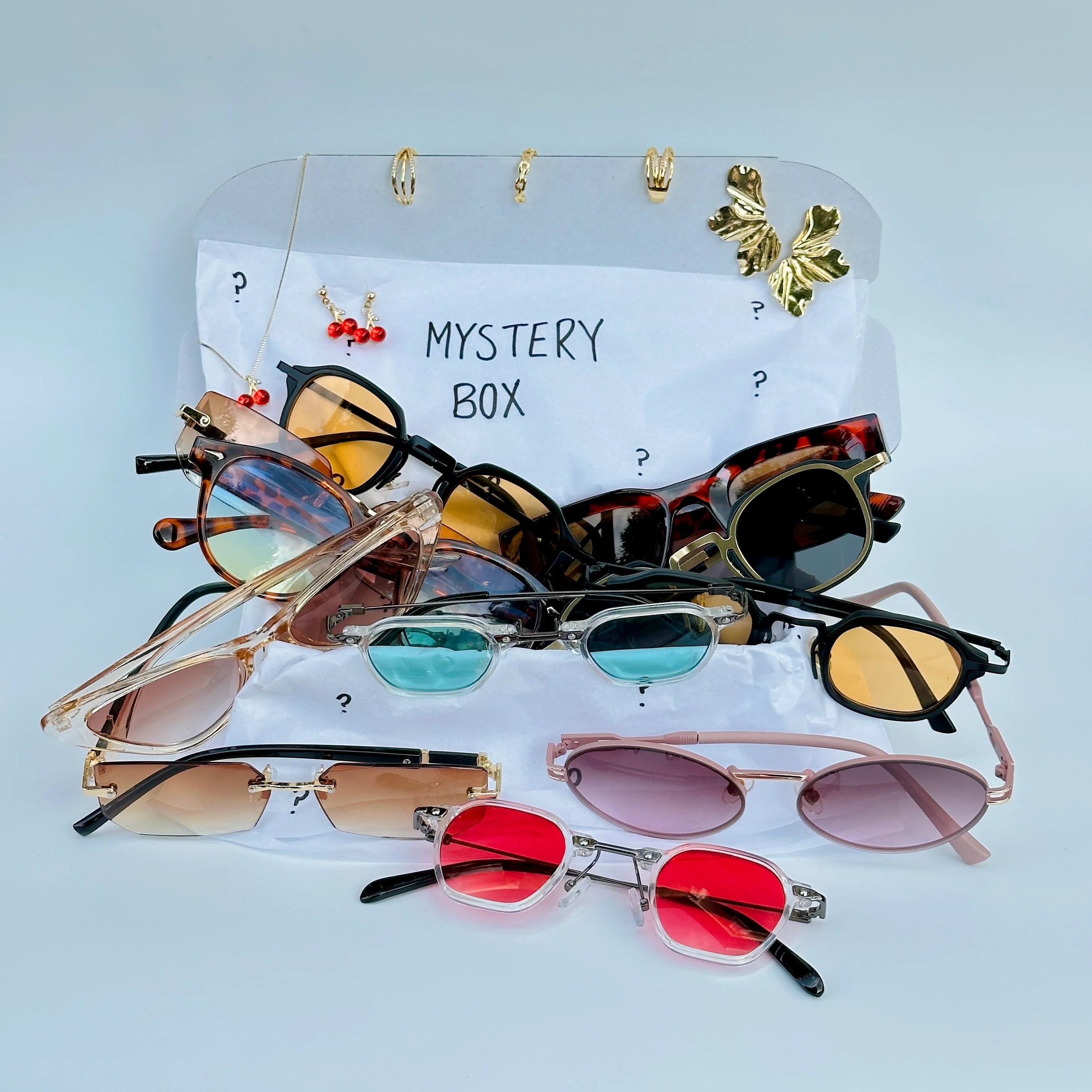 Collection of colorful sunglasses on a card labeled 'Mystery Box' against a light blue background.