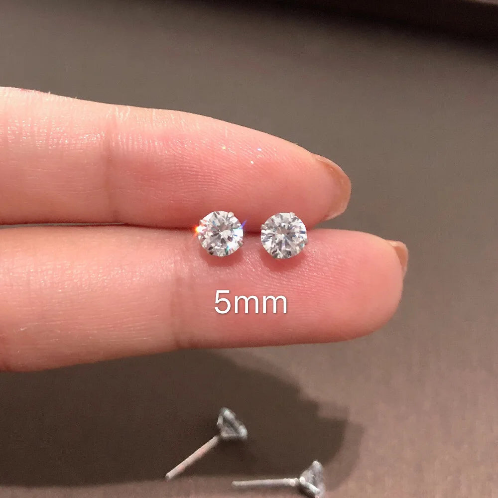 Diamond earrings held between fingers with '5mm' label on a neutral background