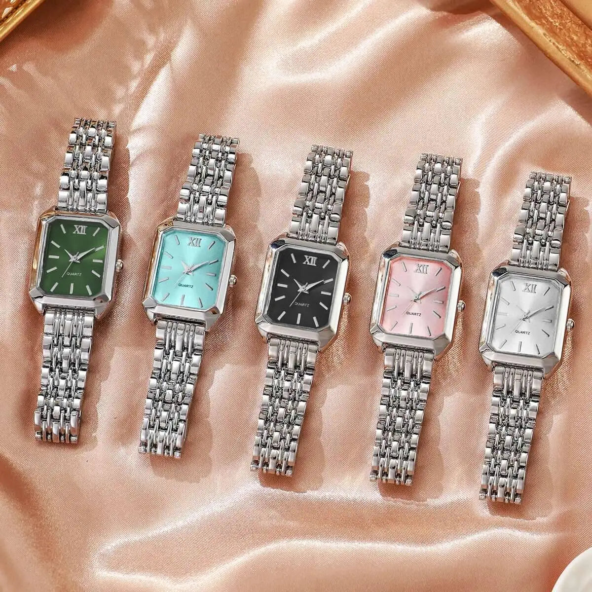 Five silver wristwatches with different colored faces on a pink fabric background