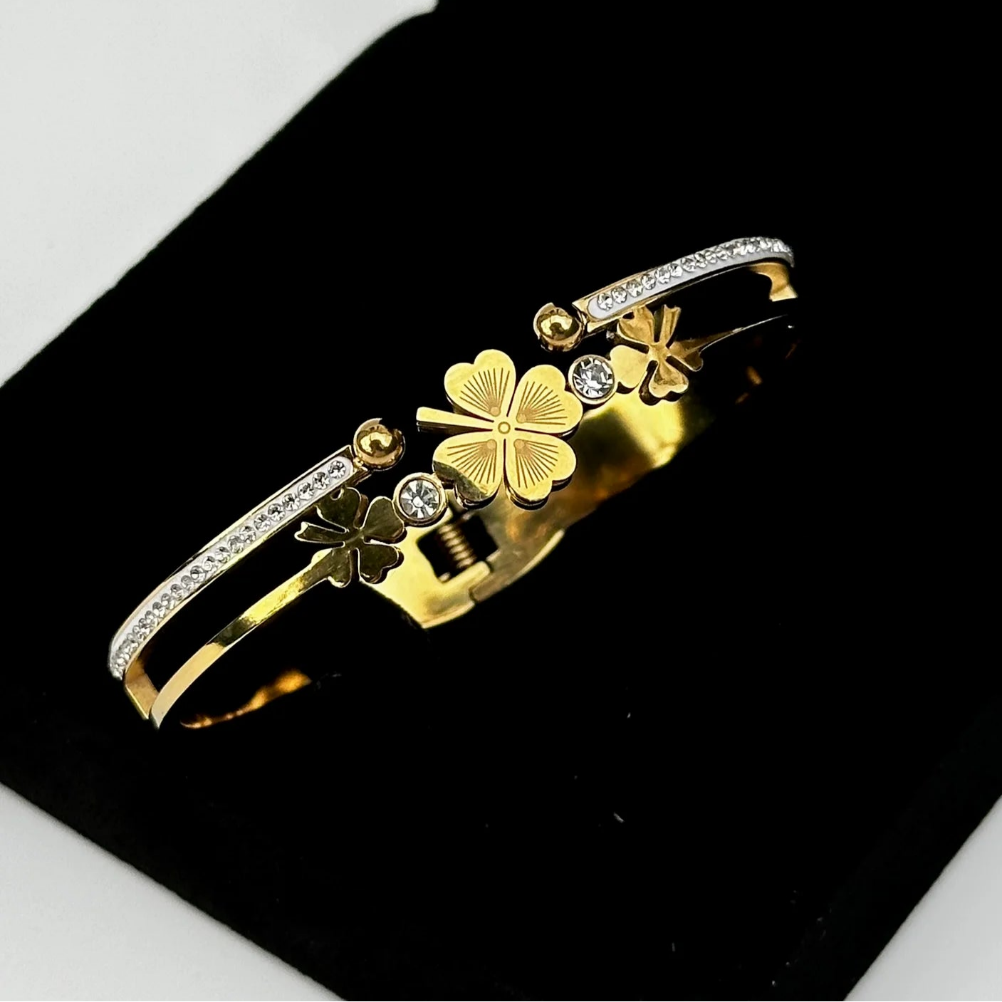 Gold bracelet with clover designs on a black stand