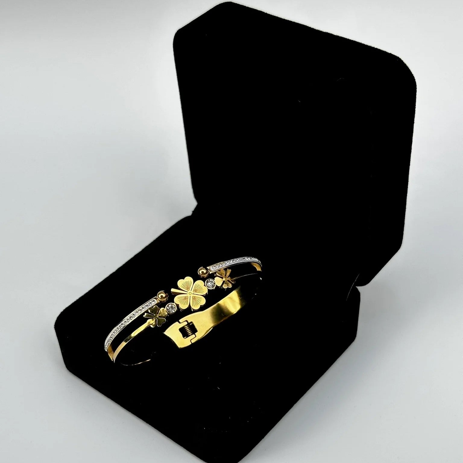 Gold bracelet with floral design in an open black jewelry box on a light gray background