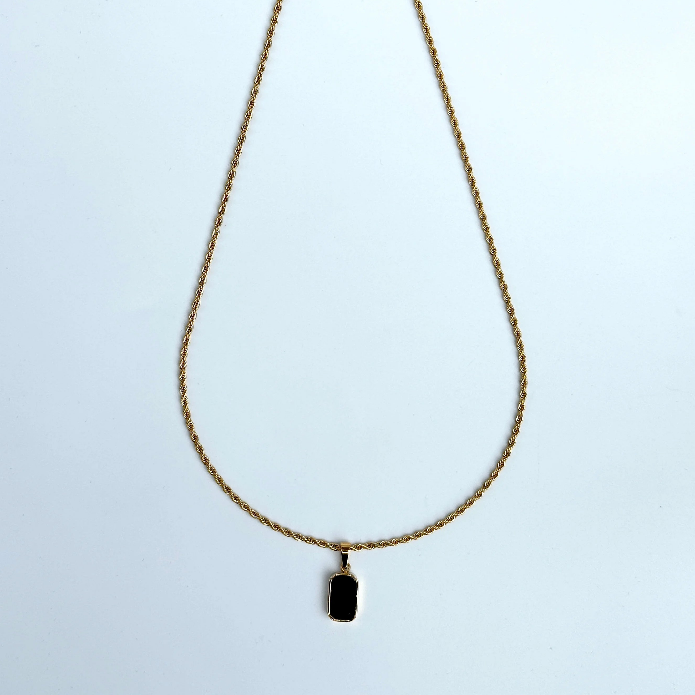 Gold necklace with a black pendant on a light blue background
