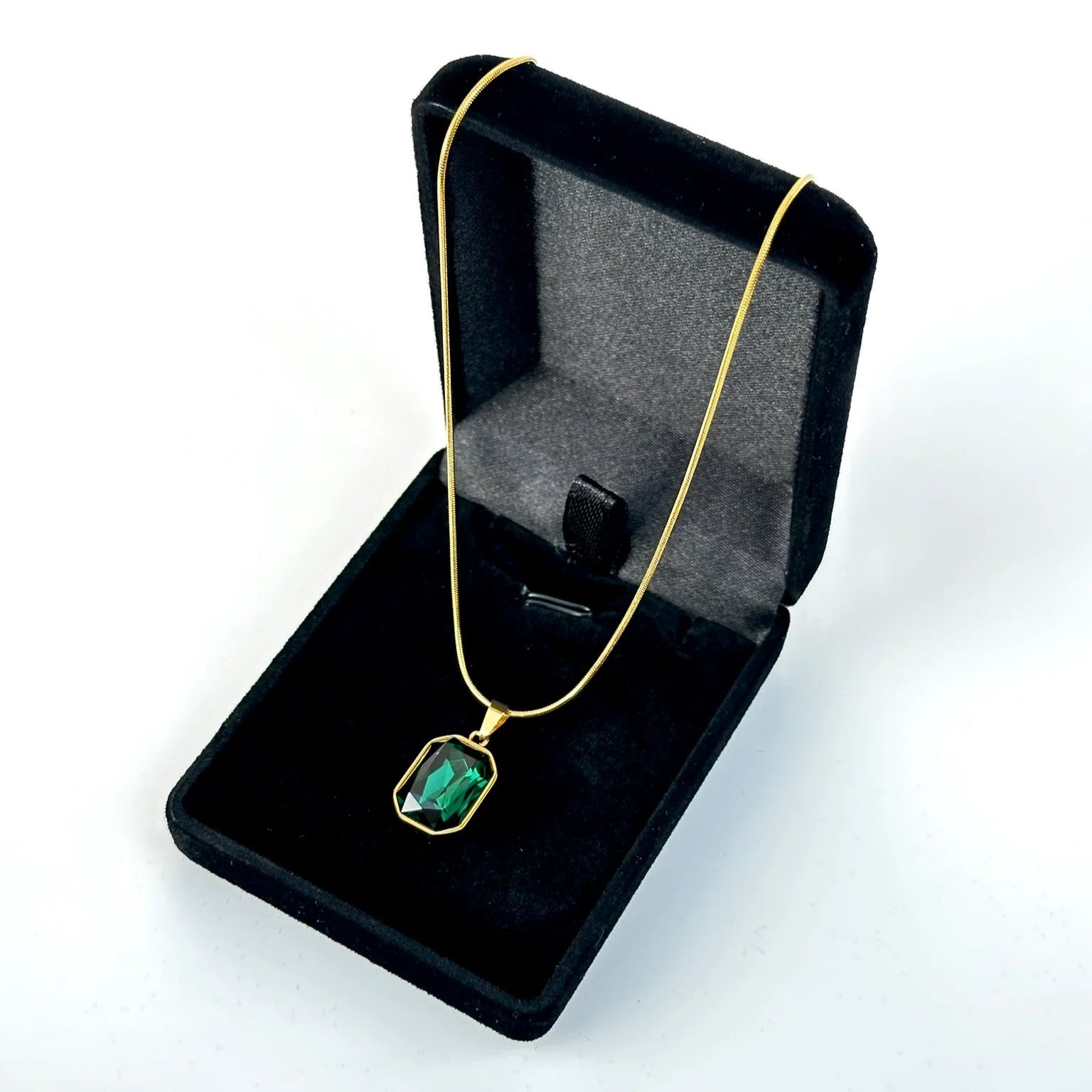 Gold necklace with a green gemstone in a black jewelry box on a white background