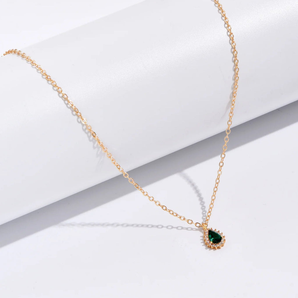 Gold necklace with a green gemstone pendant on a white surface