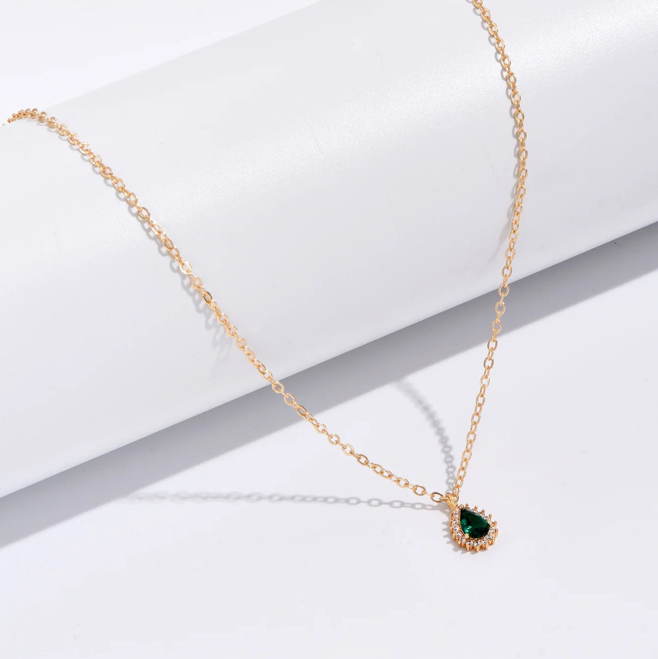 Gold necklace with a green gemstone pendant on a white surface