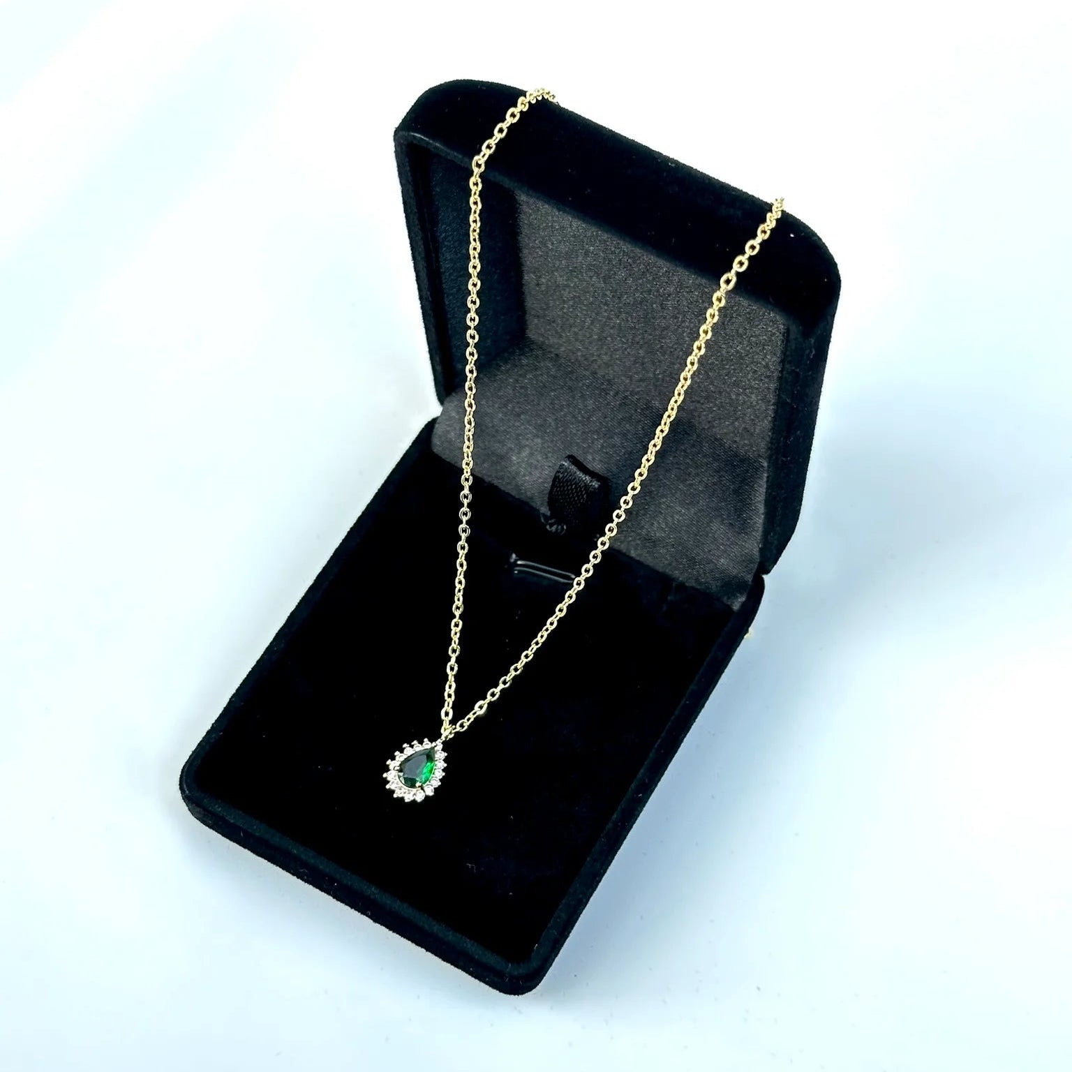 Gold necklace with a green pendant in a black jewelry box on a white background