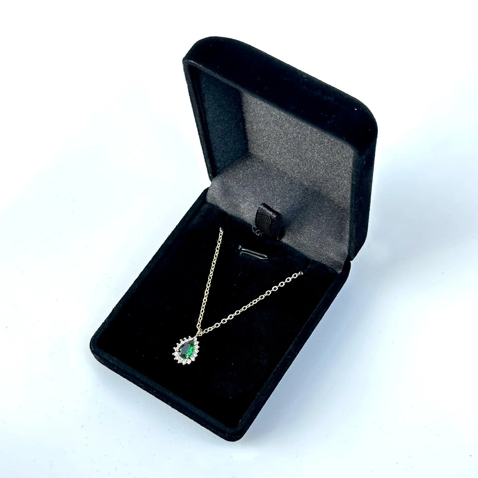 Gold necklace with a green pendant in an open black jewelry box on a white background