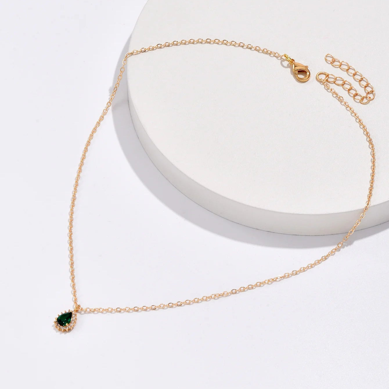 Gold necklace with a green pendant on a white background