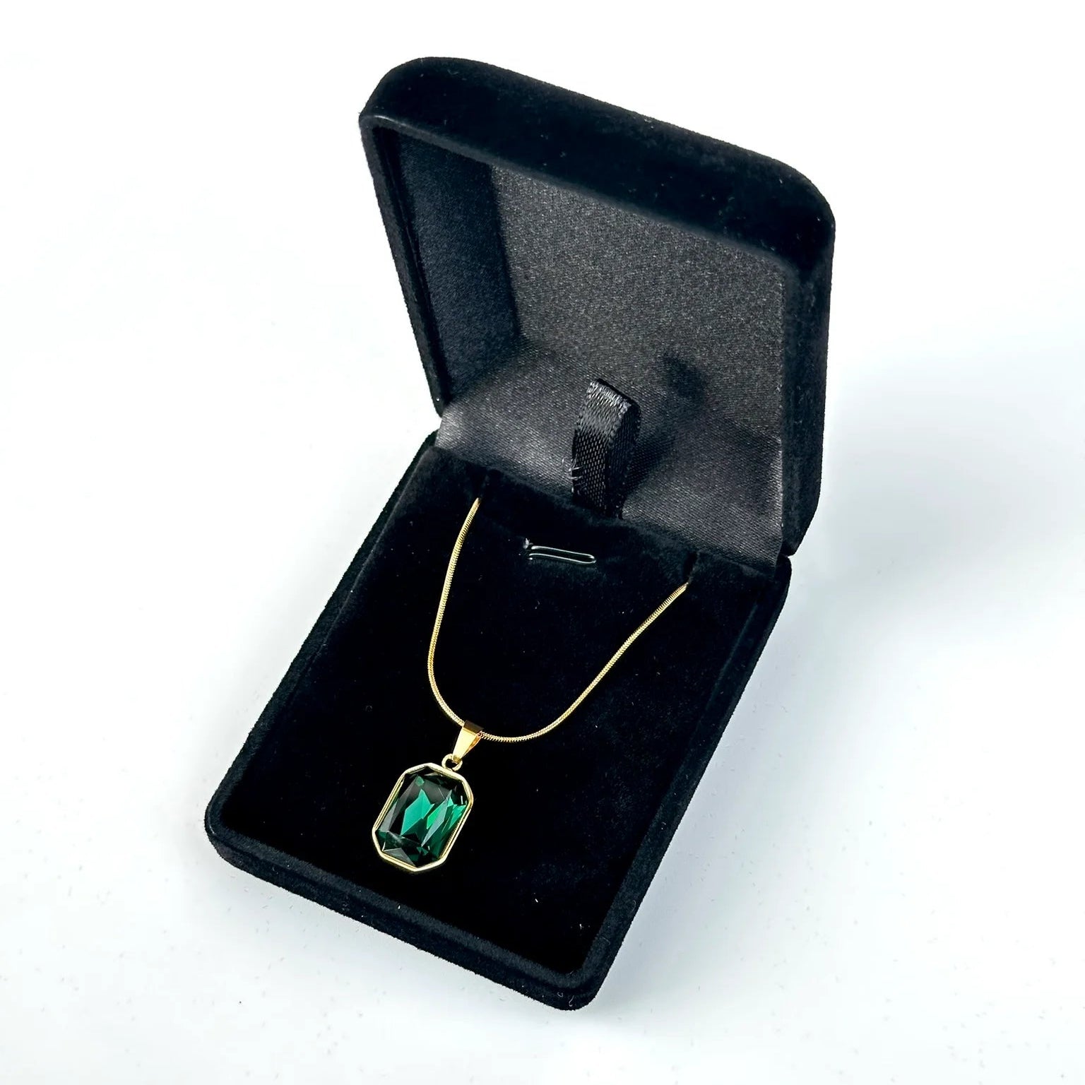 Gold necklace with a green pendant in an open black jewelry box on a white background