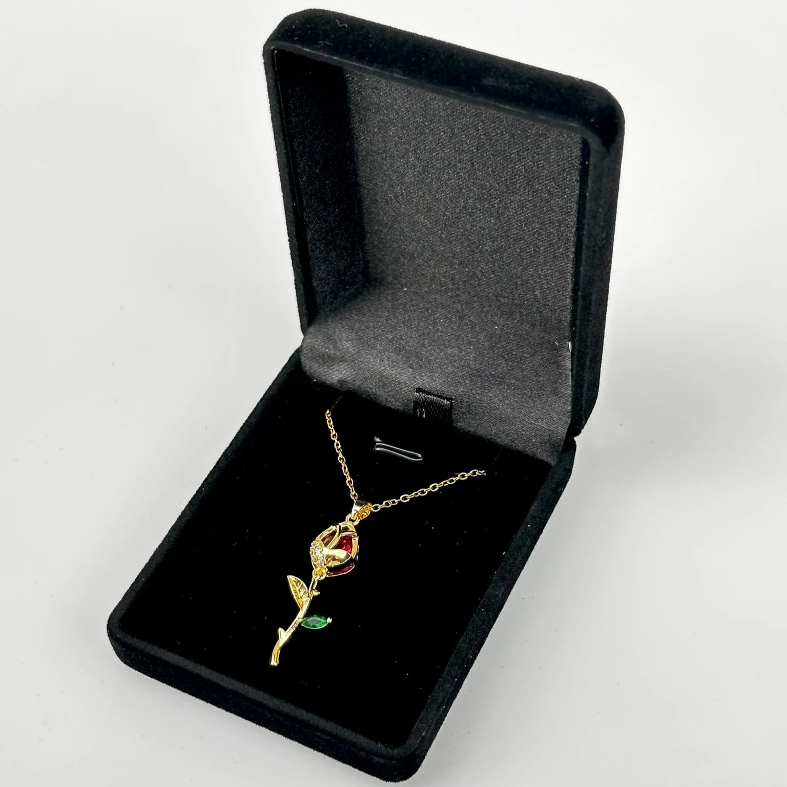 Gold rose-shaped necklace with a red gemstone in a black jewelry box on a white background