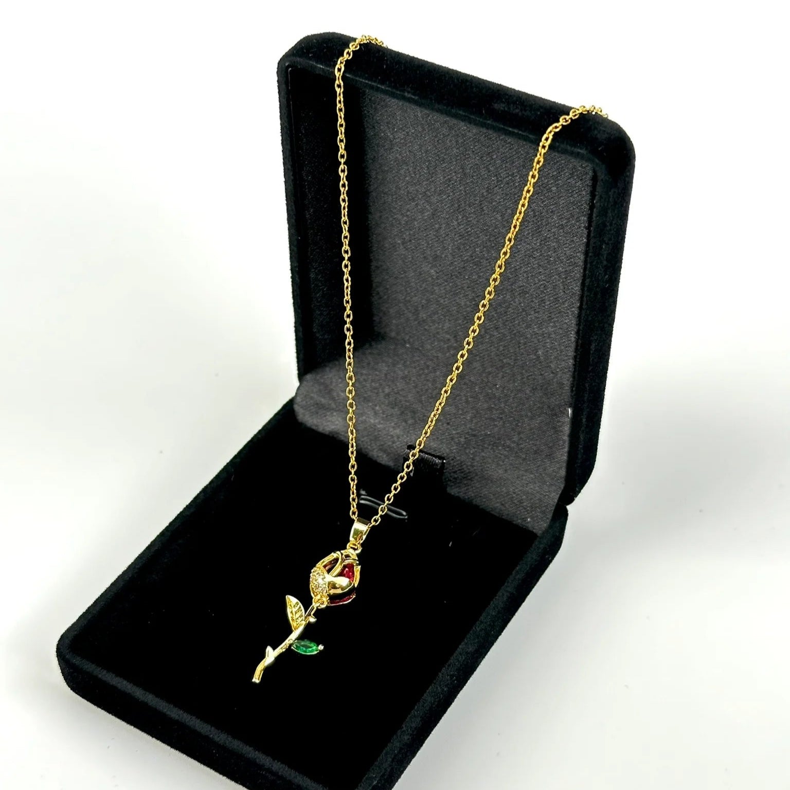 Gold rose-shaped pendant necklace in a black jewelry box on a white background