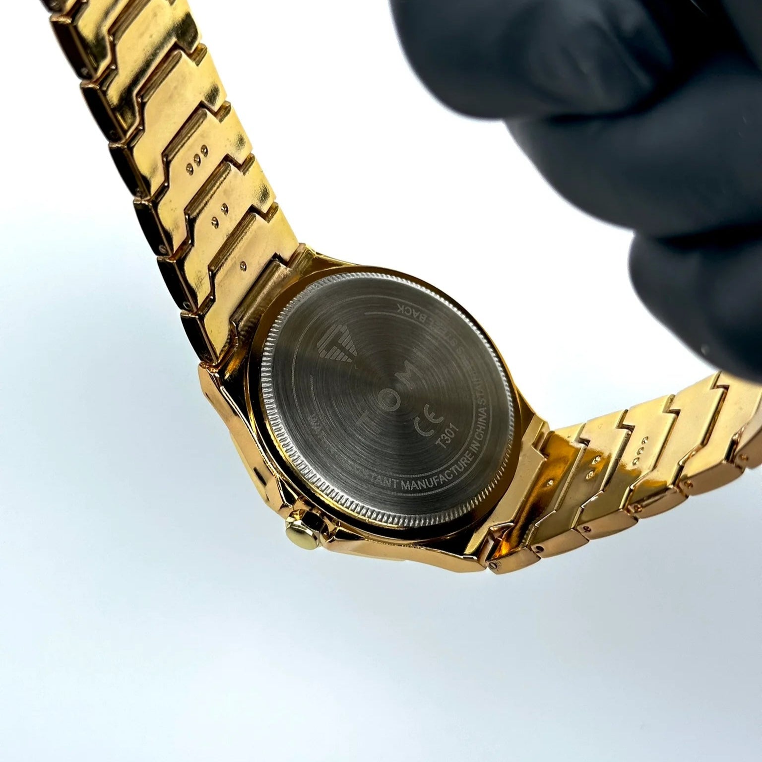 Gold watch with a textured face held by a gloved hand on a light blue background