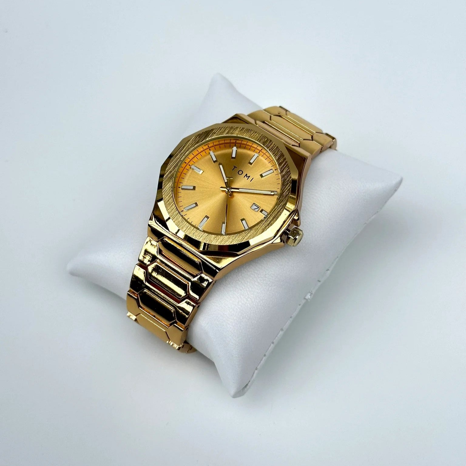 Gold wristwatch on a white cushion with a white background