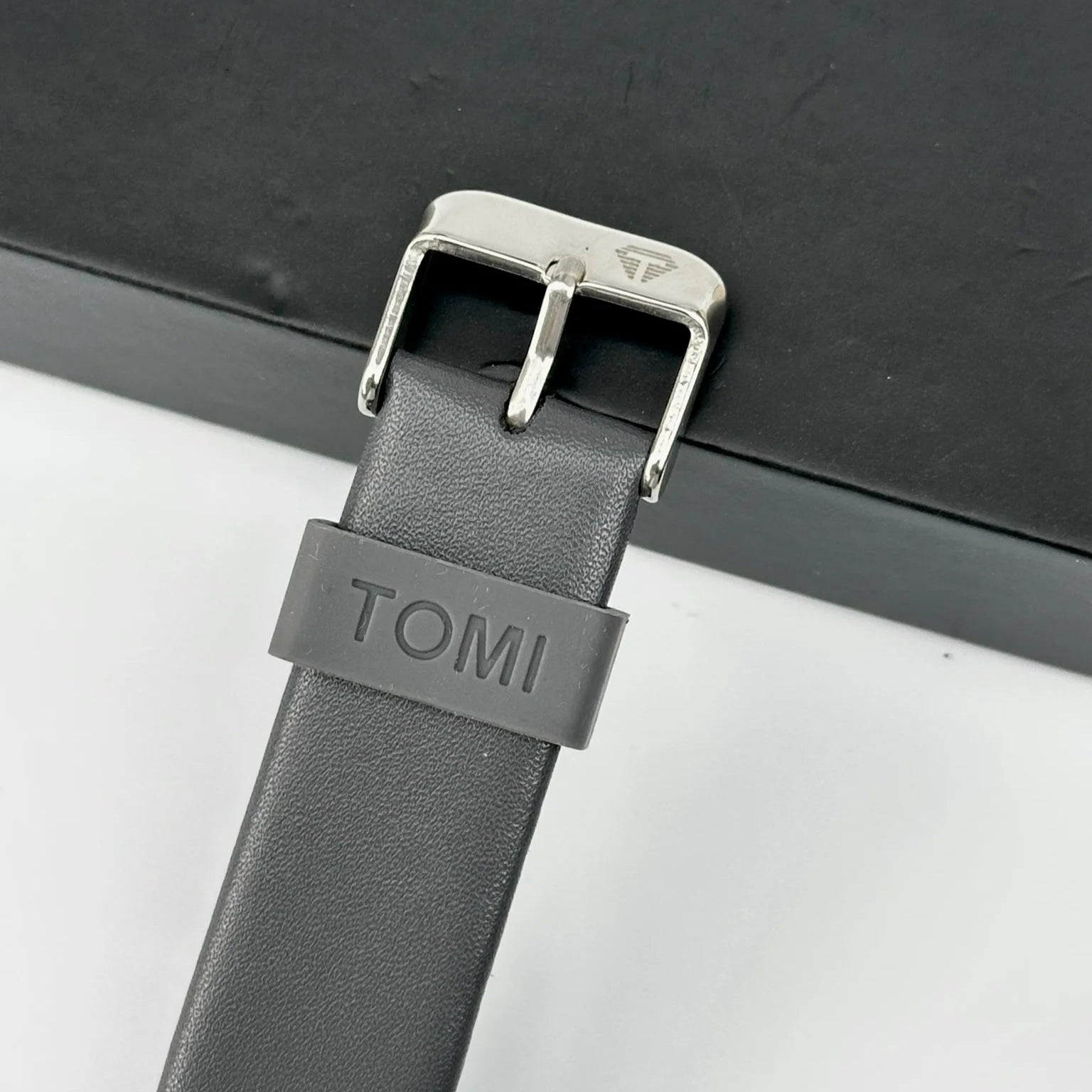 Gray leather strap with silver buckle on a black surface