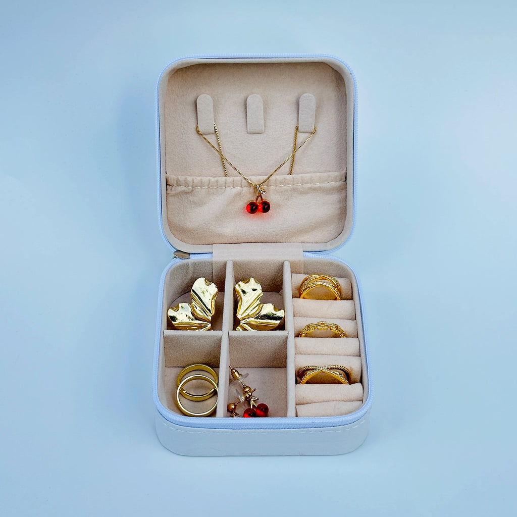 Jewelry set including a necklace with a red pendant, earrings, and rings in an open jewelry box on a light blue background.