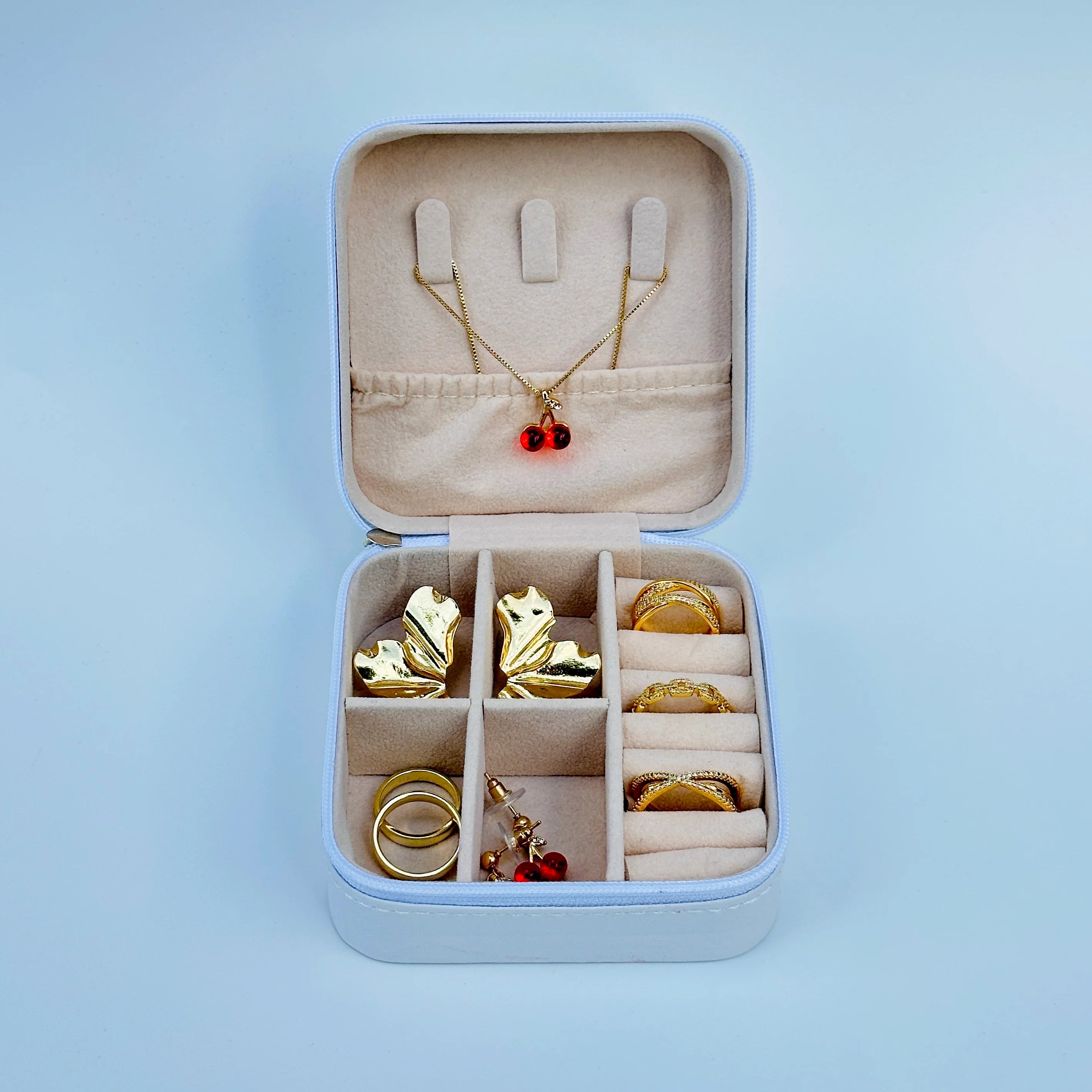 Jewelry set including a necklace with a red pendant, earrings, and rings in an open jewelry box on a light blue background.
