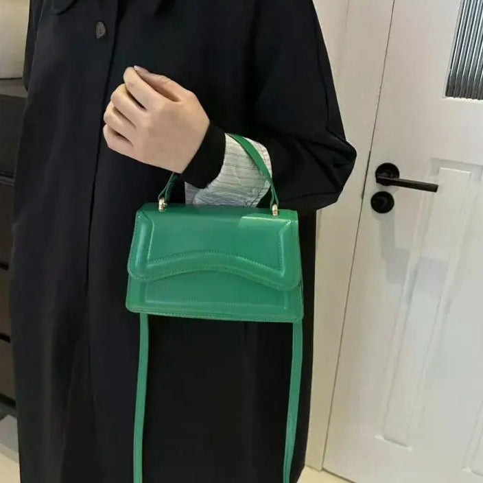Person holding a green handbag in front of a white door