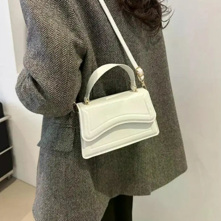 Person wearing a gray coat with a white handbag over their shoulder against a plain background