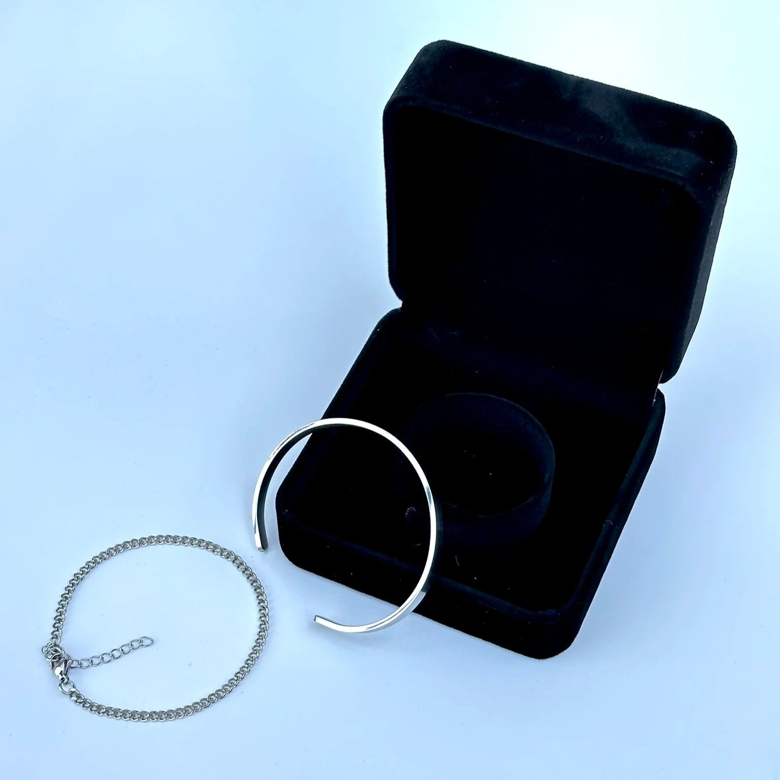 Silver bracelet on a light blue background with an open black jewelry box.