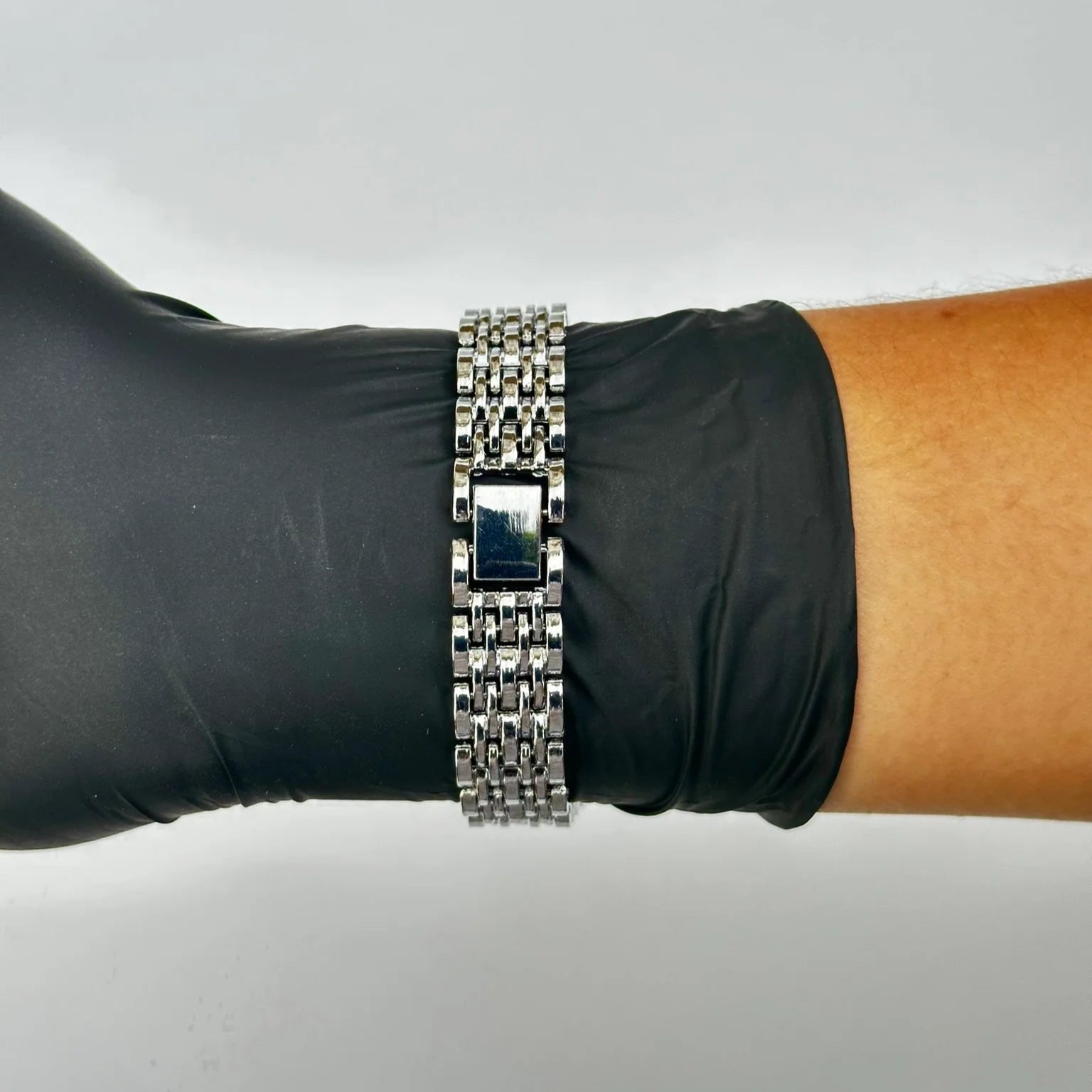 Silver bracelet on a wrist with a black glove against a gray background