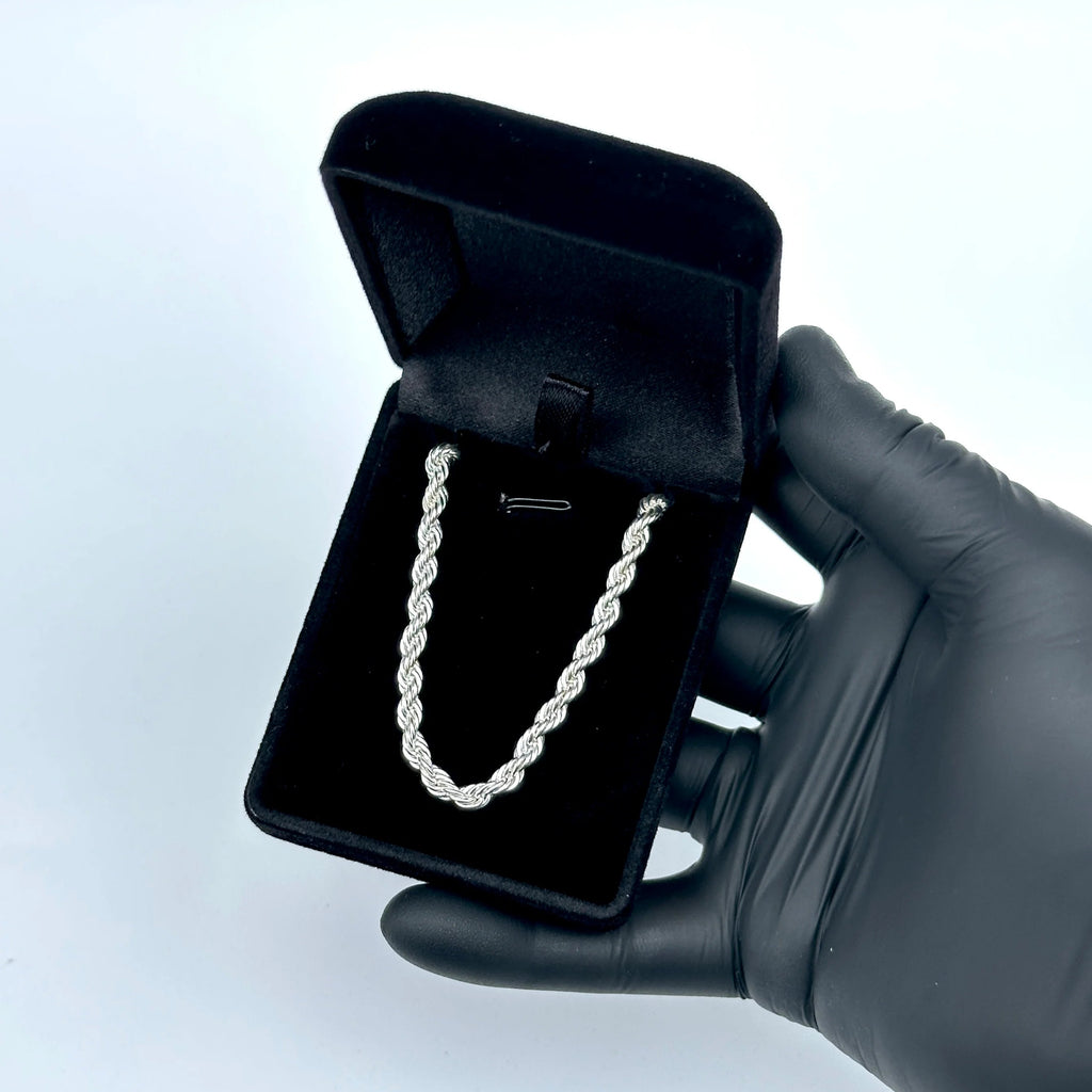 Silver chain necklace in a black jewelry box held by a gloved hand on a light blue background