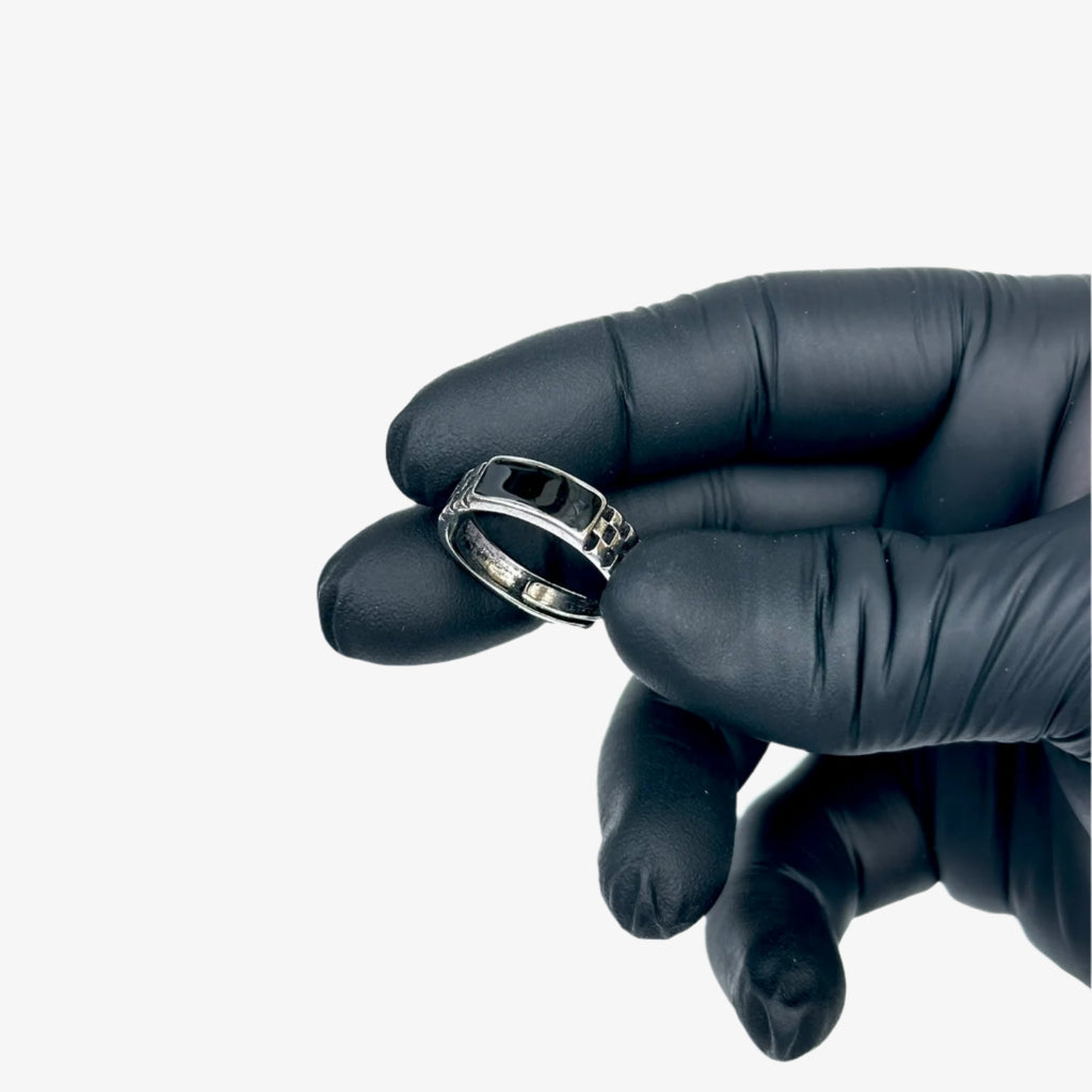 Silver ring held by a gloved hand against a light blue background