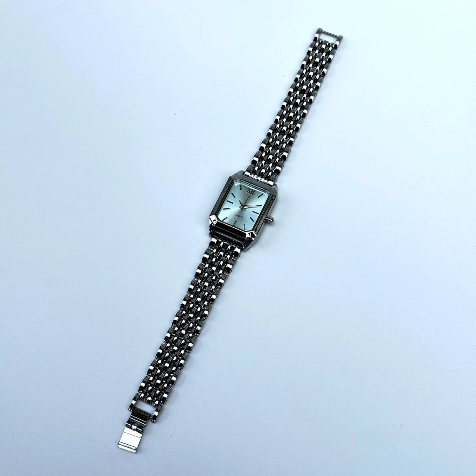 Silver watch with a chain strap on a light blue background