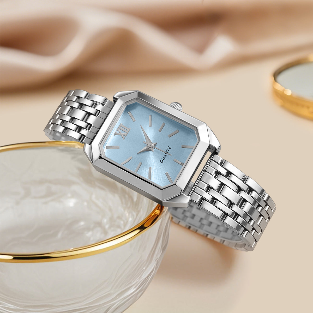 Silver watch with a light blue face on a beige fabric background