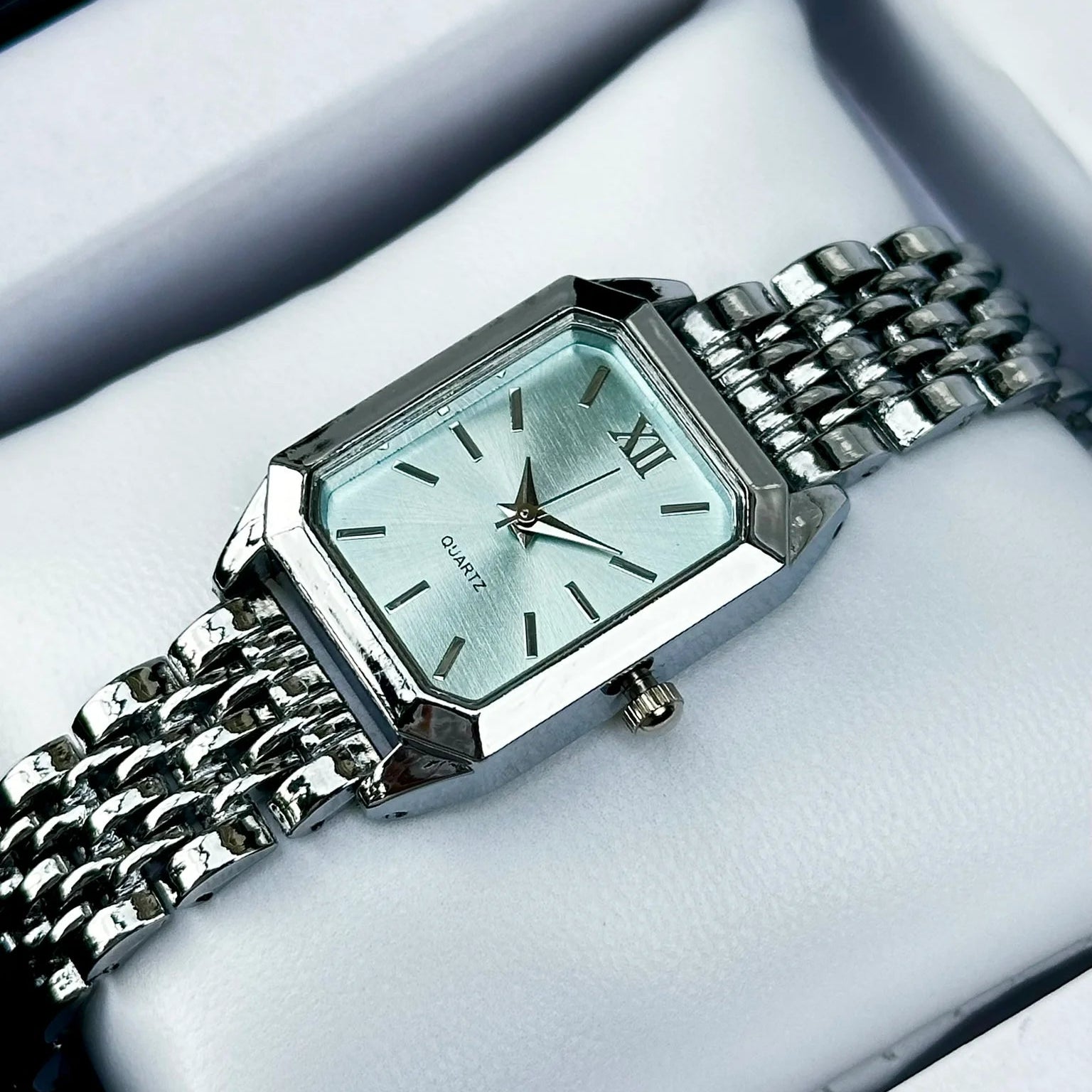 Silver watch with a light green face on a white cushion
