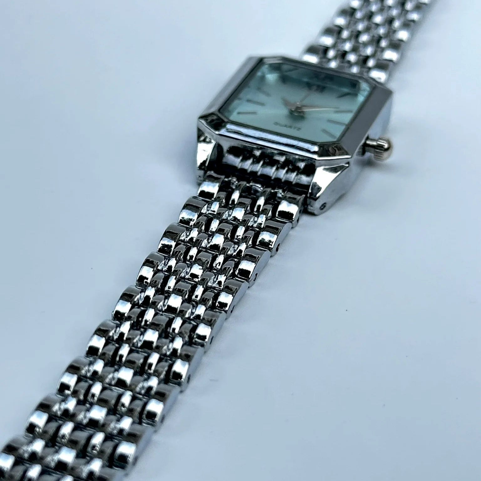 Silver watch with a mesh band on a light gray background