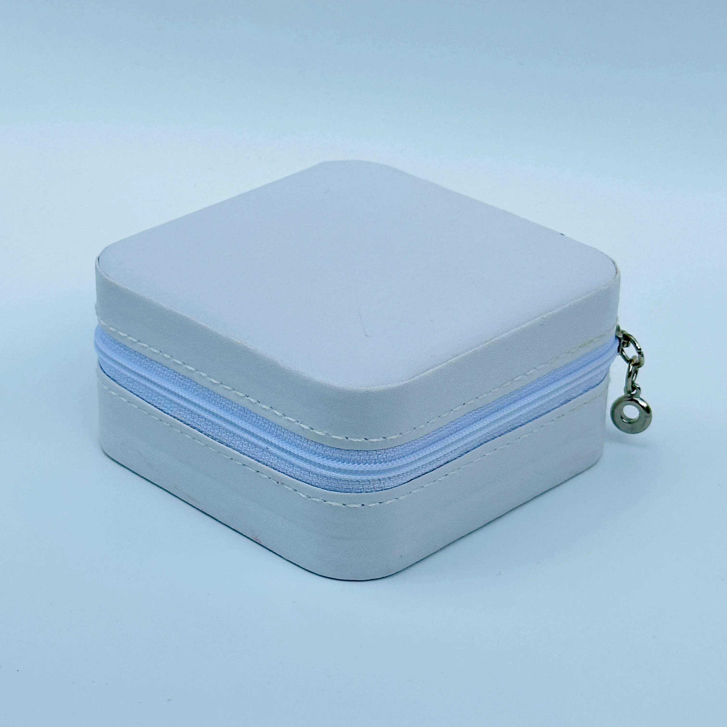 Small square jewelry box with a light blue zipper on a light blue background