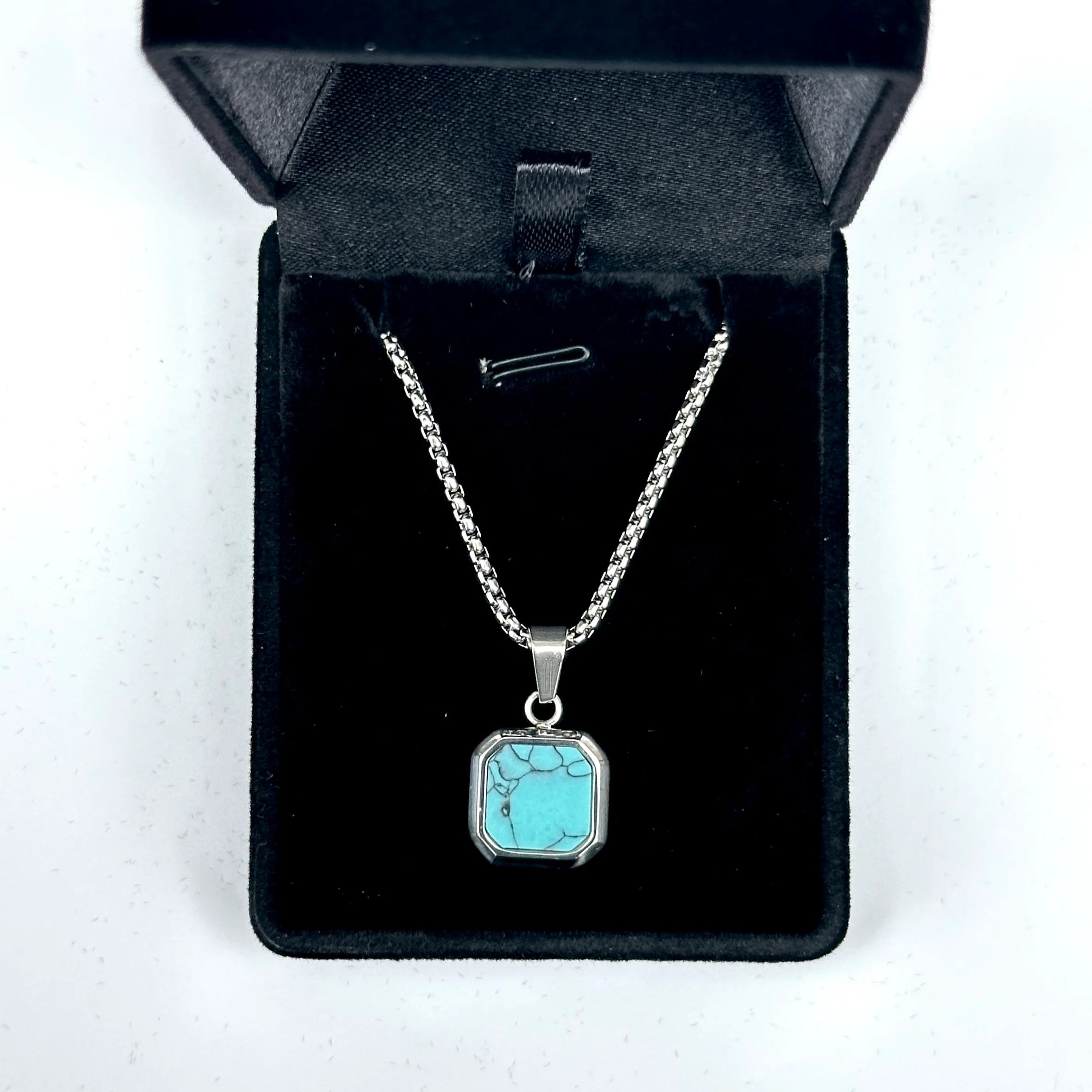 Turquoise pendant necklace in a black jewelry box on a white background