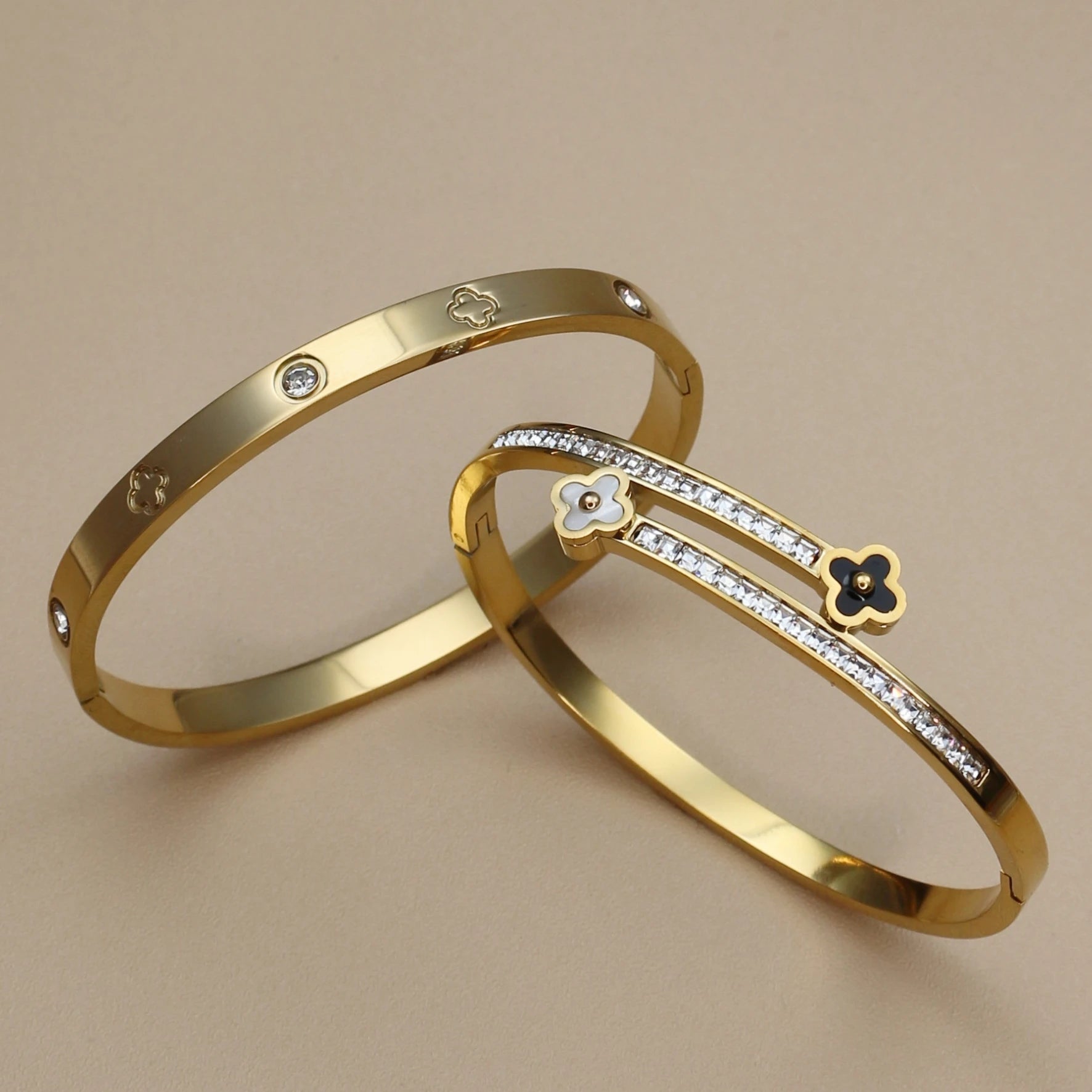Two gold bracelets with diamond accents on a beige background