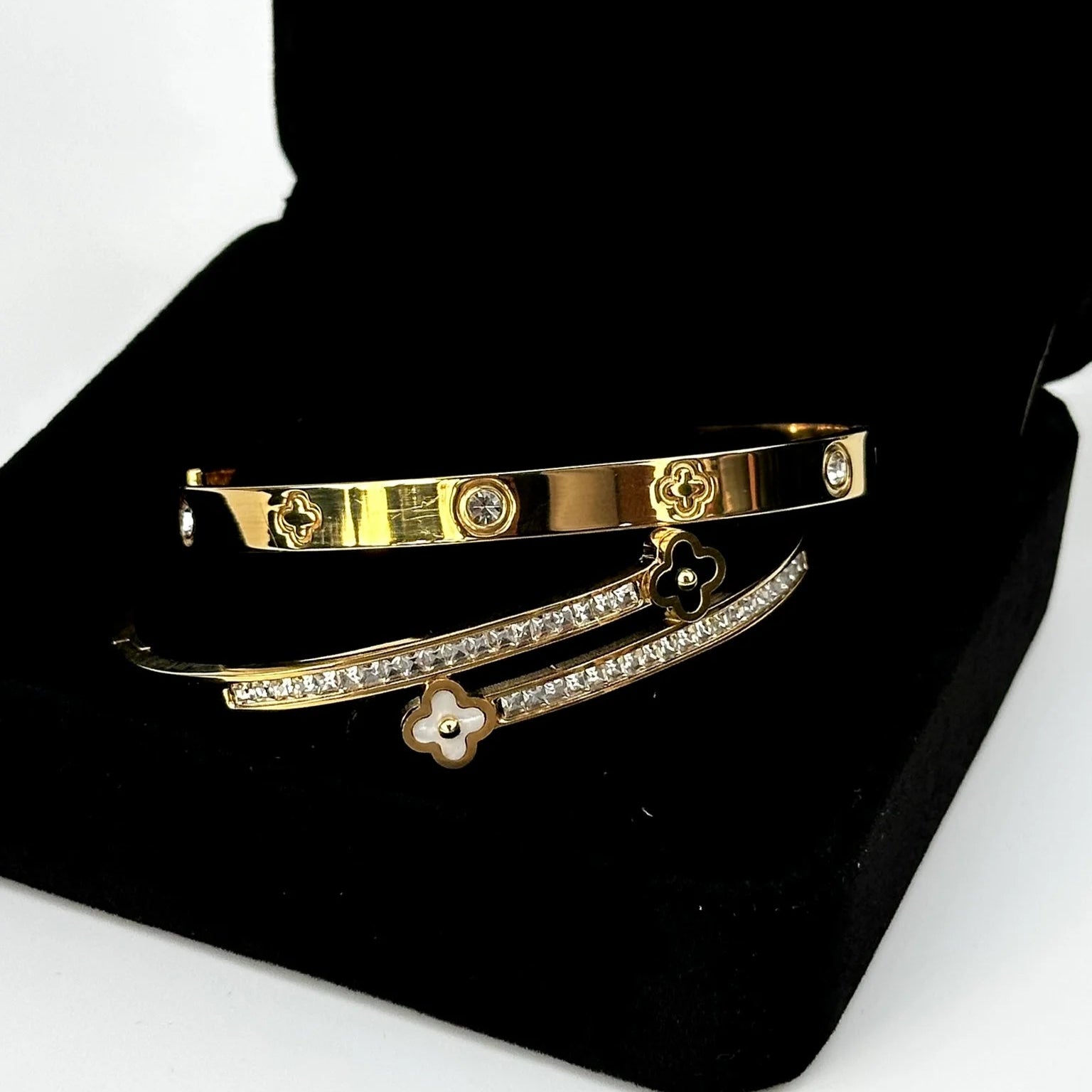 Two gold bracelets with diamond accents on a black stand.