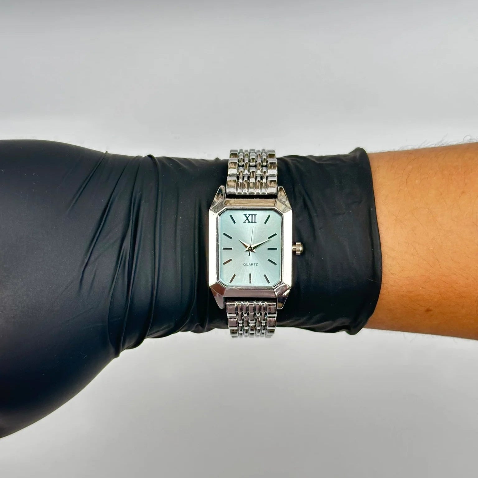 Watch on a wrist with a black glove against a gray background