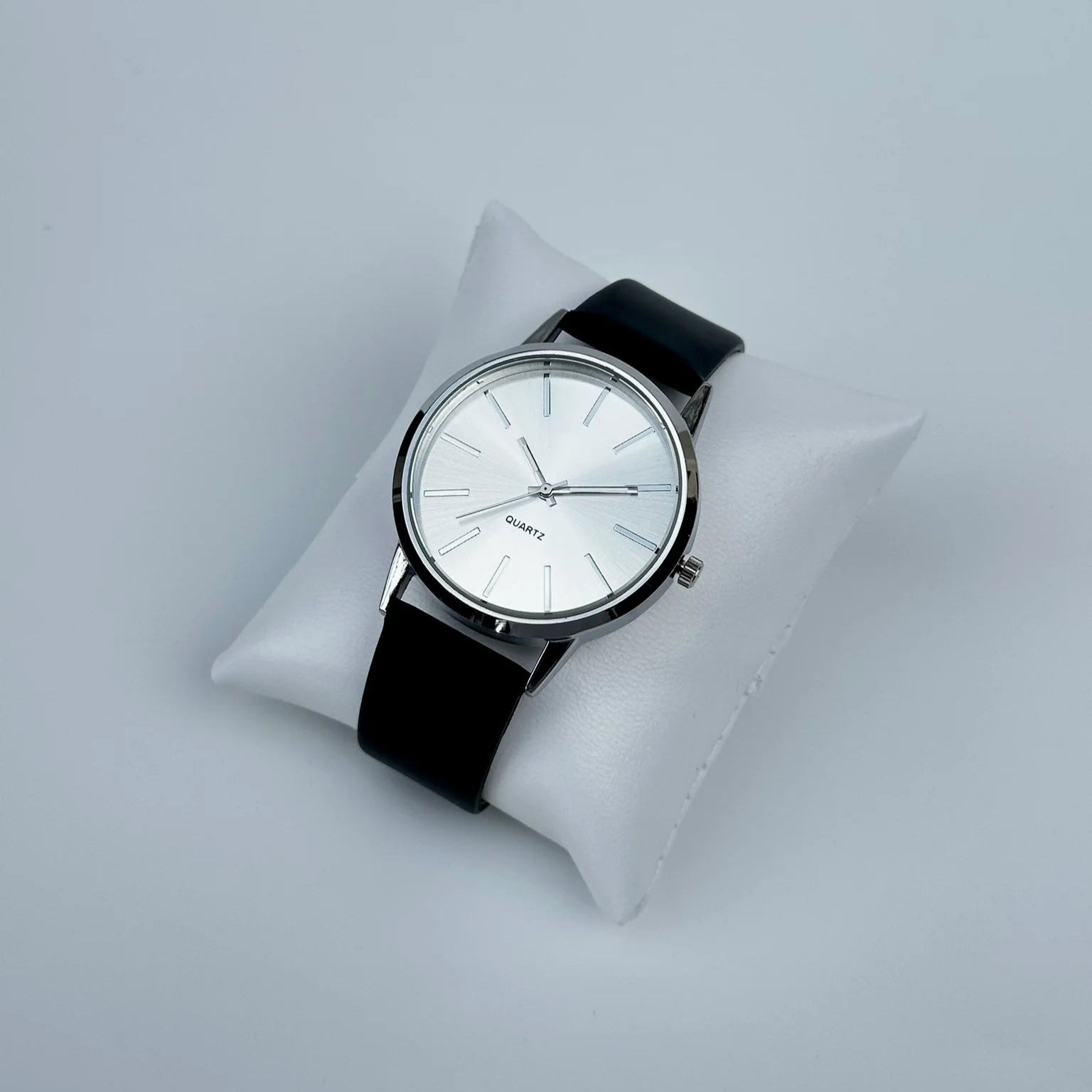 Watch with a black strap on a white cushion against a light gray background