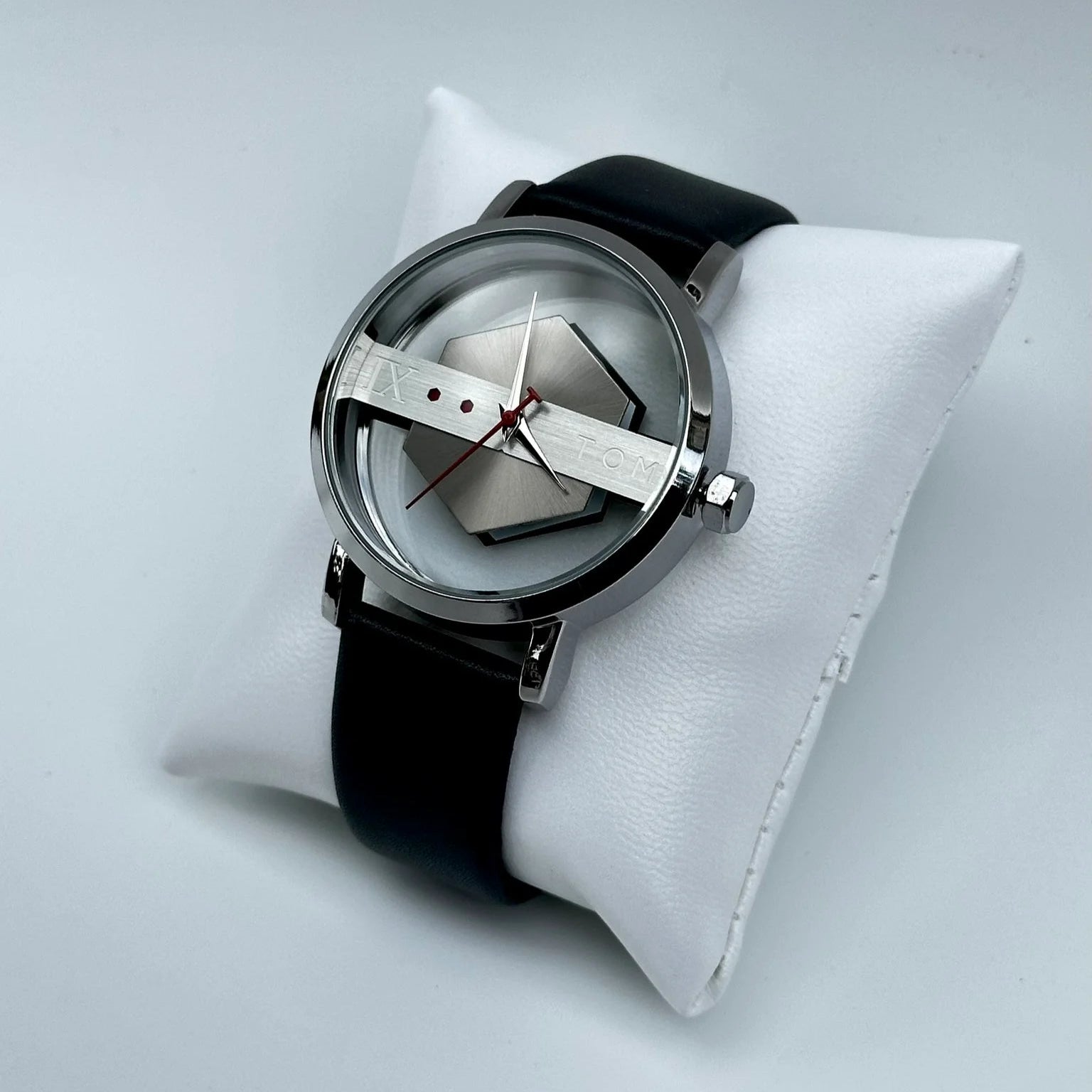Watch with black strap and silver case on a white cushion against a light gray background