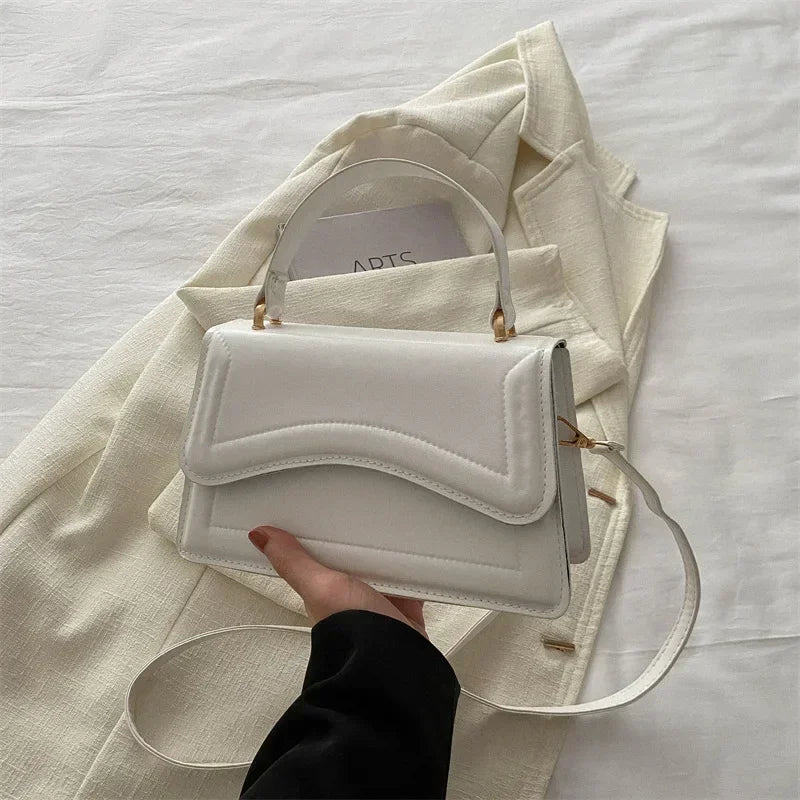 White handbag held by a hand on a light fabric background